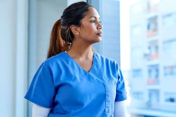 Nurse in blue scrubs looking out of a hospital window
