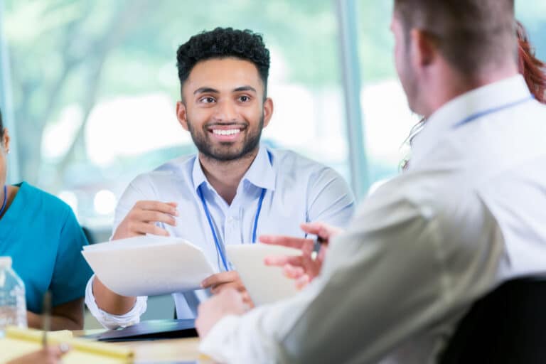 Young Indian male doctor discusses a patient's case with colleagues. They are reviewing the patient's medical chart.